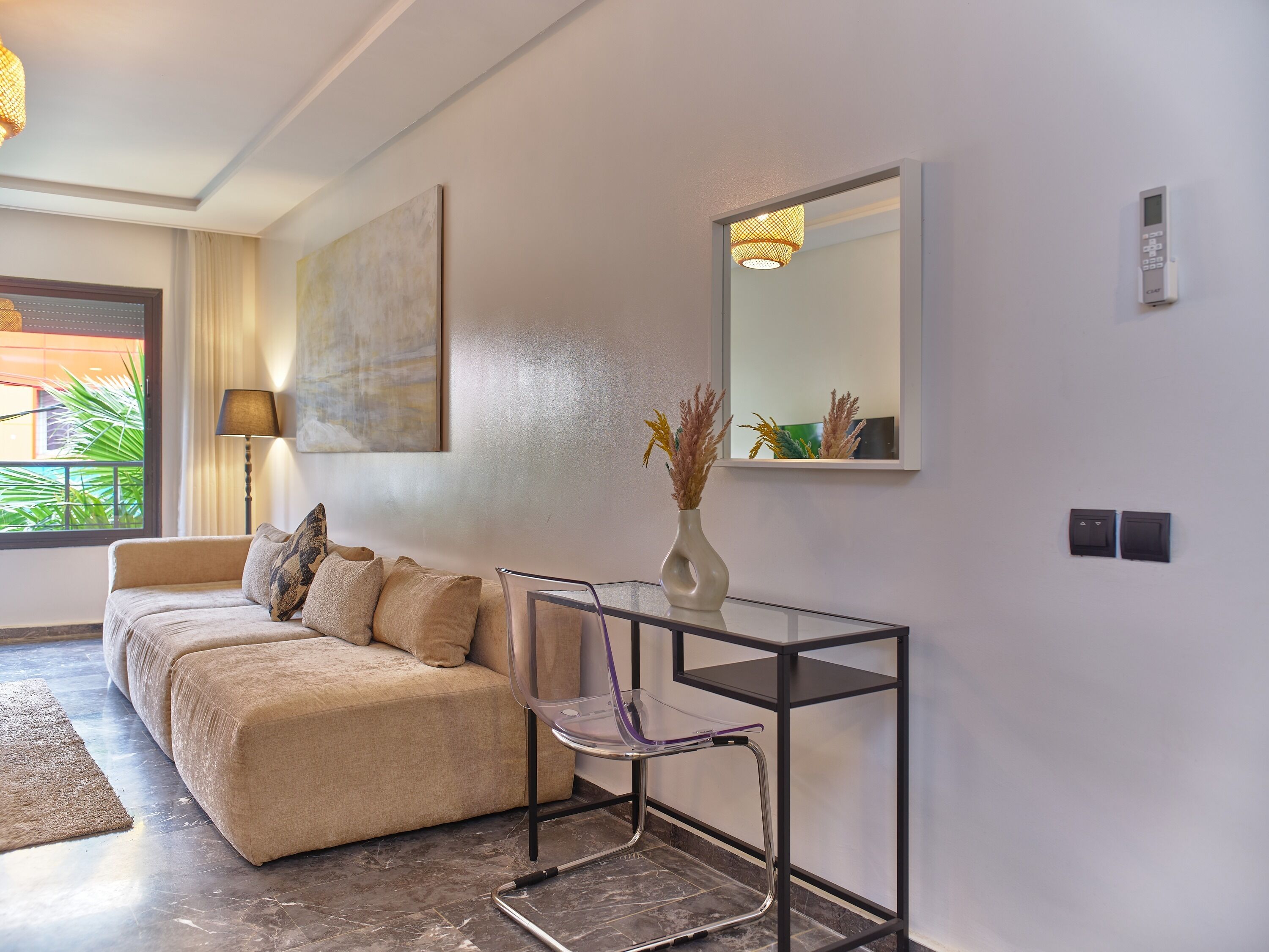 A modern living room with a sofa, a glass table, a vase with dried flowers, a lamp, and a large painting on the wall.
