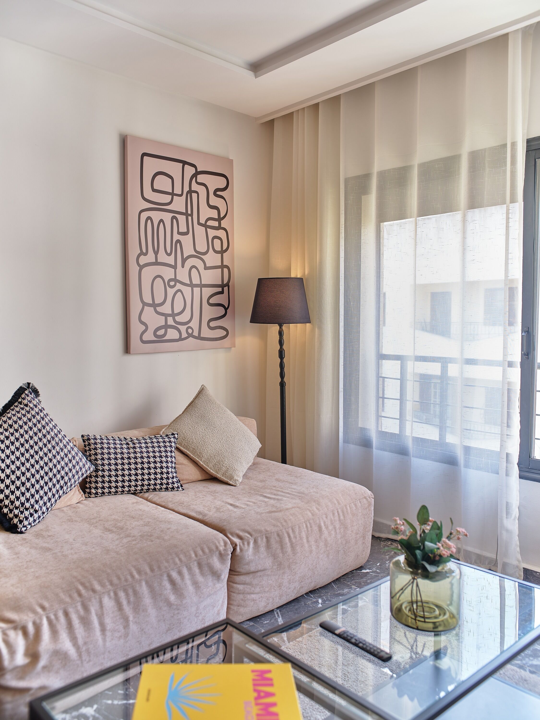 Una sala de estar moderna con un sofá color beige, cojines decorativos, una lámpara de pie y una mesa de centro de vidrio con un florero.