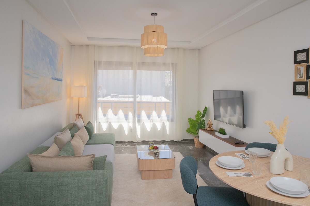 Ein modernes Wohnzimmer mit Sofa, Couchtisch, Esstisch für vier Personen und Fernseher.