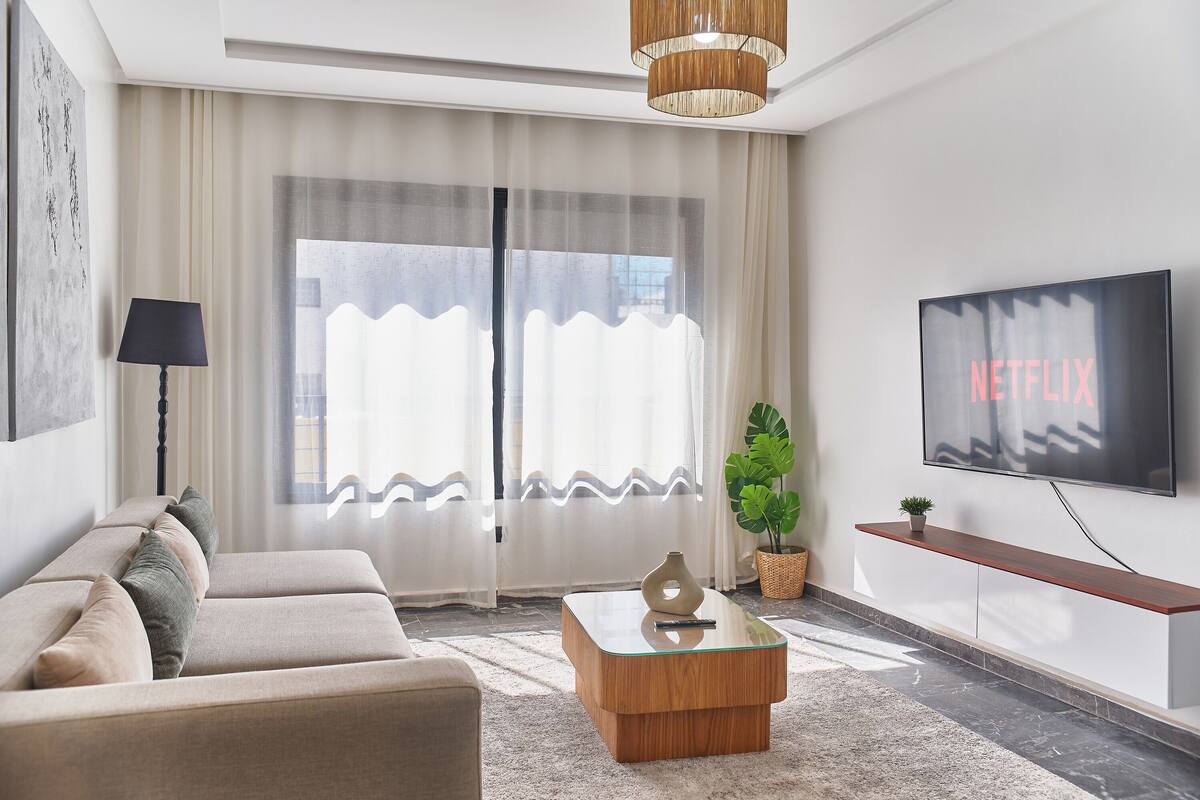 Ein modernes Wohnzimmer mit einer Couch, einem Couchtisch und einem Fernseher, der 'NETFLIX' zeigt.