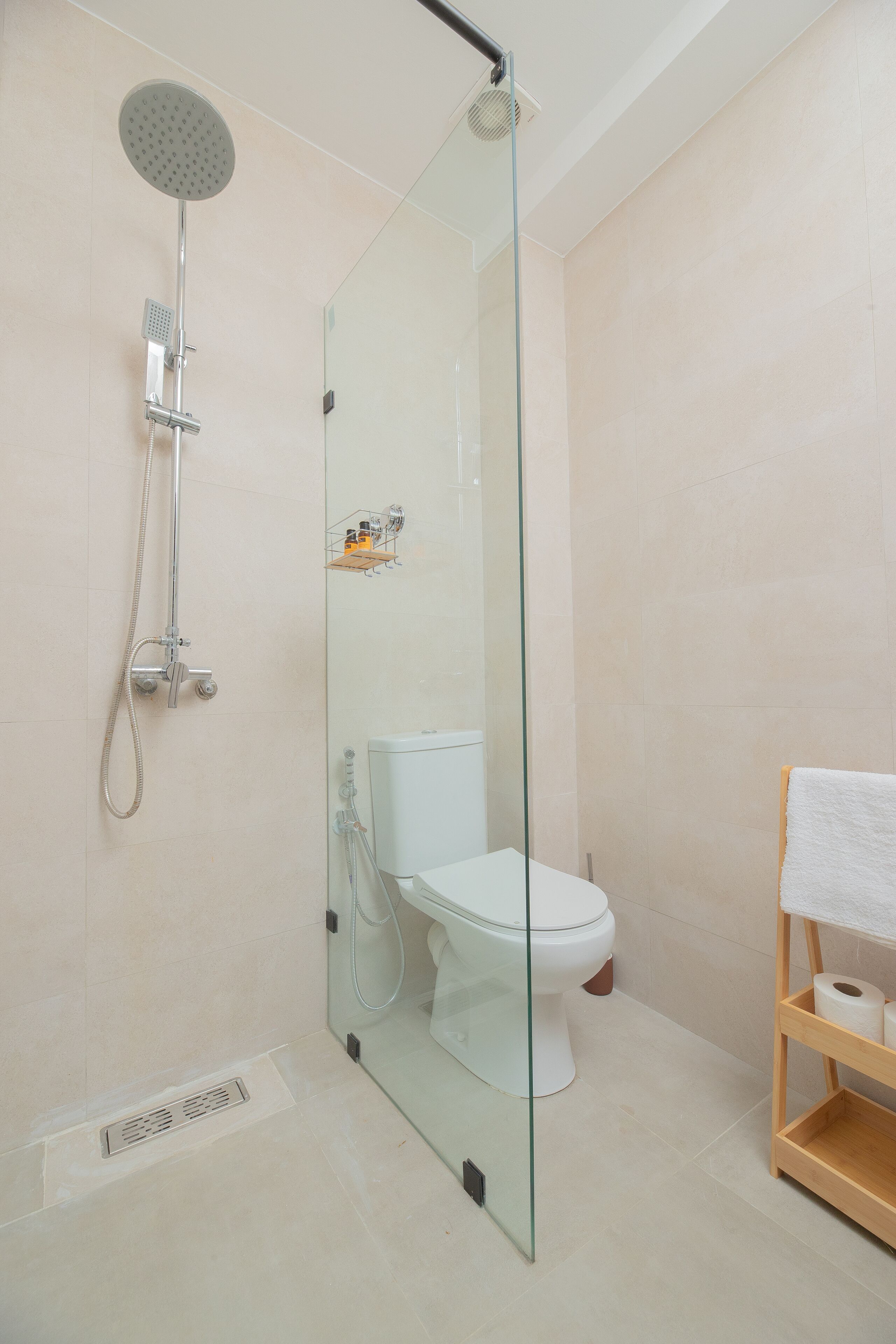 A modern bathroom with a glass-enclosed shower, a toilet, and a wooden shelf with towels.