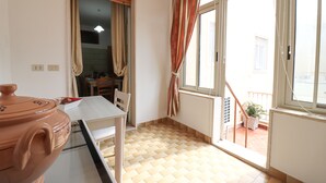 A room with a dining table, chairs, a large window with curtains, a radiator, and a potted plant. - Isabel's house in Otranto 10 seats (Otranto)
