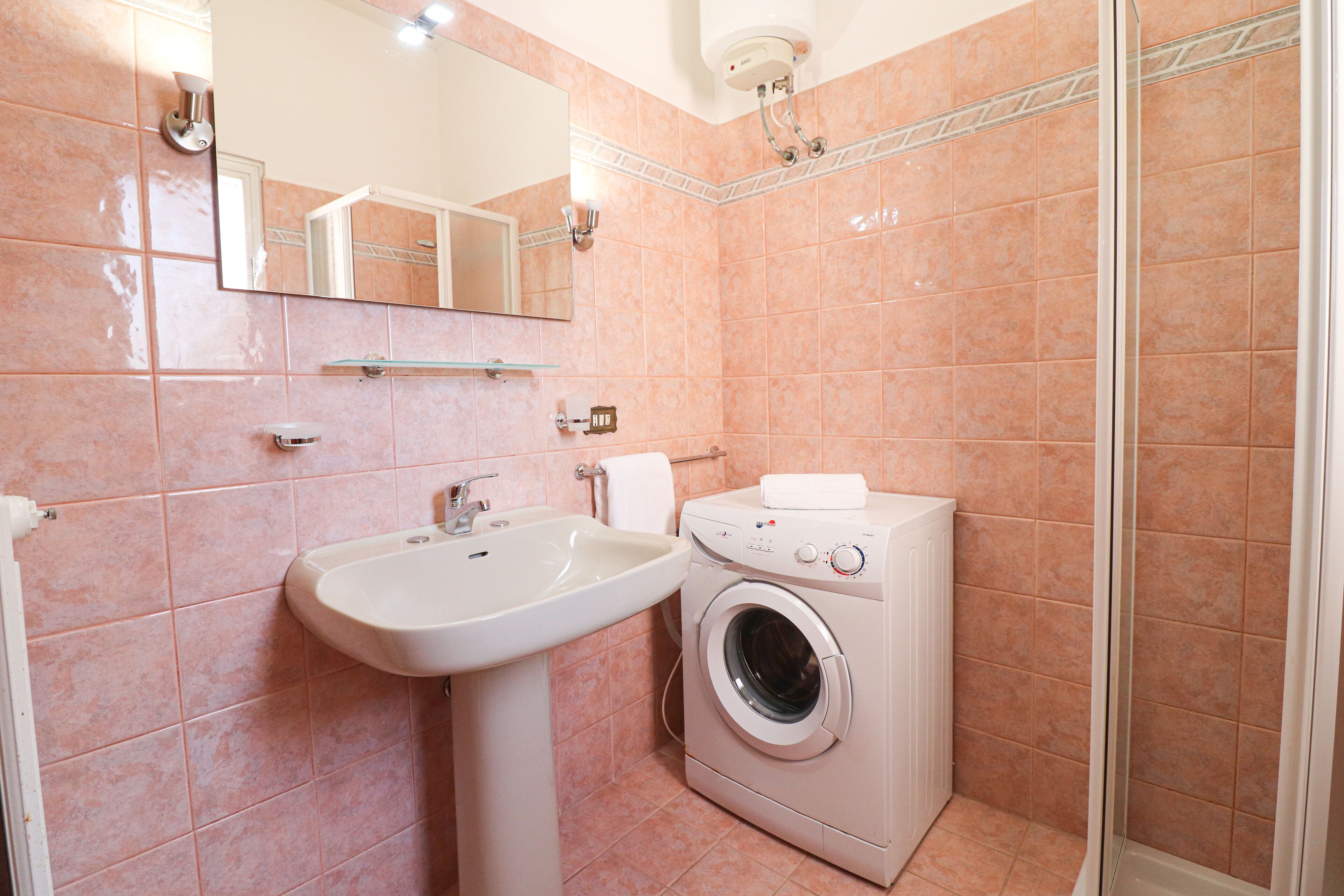 Baño con lavamanos, espejo y lavadora.