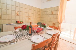 Uma área de refeições com painel de azulejos, uma mesa posta para quatro com pratos, copos e uma garrafa de vinho.