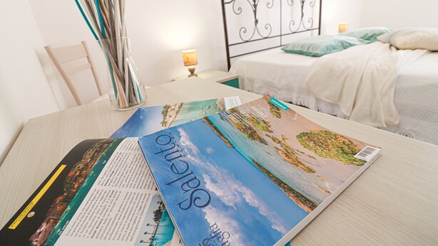 A neatly made bed with white linens, a bedside table with a lamp, and a magazine on the table. - Isabel's house in Otranto 10 seats (Otranto)