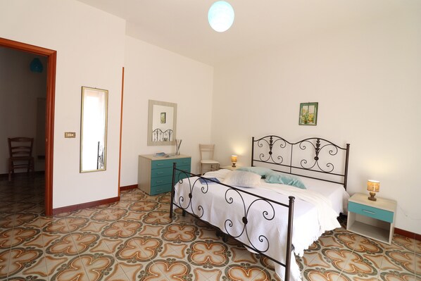 A bedroom with a bed, a nightstand, a dresser, a chair, and a mirror.