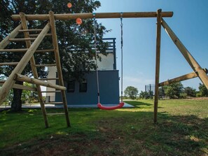 Un’altalena in legno su un prato, con un edificio sullo sfondo.