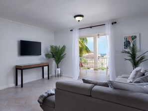 Relax in this spacious living room with a large sofa, flat-screen TV, and sliding door to an ocean-view outdoor area.