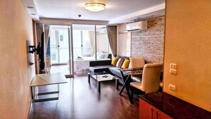 A modern hotel room with a sofa, a small table, a balcony with a bed, and a brick accent wall. - Short-Term Rental Allowed - 6D Downtown Bkk Serviced Apartment (Krung Thep Maha Nakhon)