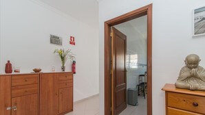 A hallway with a wooden cabinet, a statue, and a door leading to another room. - Cabanas T1 Apartment with Balcony & BBQ – 8min Walk to Beachfront (Faro)