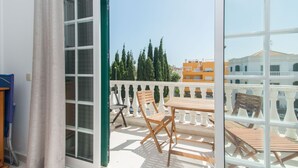 A balcony with a wooden table and chairs, a view of trees and buildings, and a white railing. - Cabanas T1 Apartment with Balcony & BBQ – 8min Walk to Beachfront (Faro)