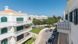 A multi-story residential building with balconies, a street view, and parked cars. - Cabanas T1 Apartment with Balcony & BBQ – 8min Walk to Beachfront (Faro)