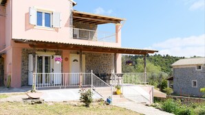 A two-story house with a balcony, a stone facade, and a small garden area.