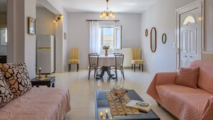 A living room with a sofa, a coffee table with a book and candles, a dining area with a table and chairs, and a chandelier.
