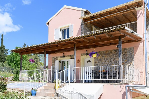 A two-story house with a balcony, stone facade, and a wooden roof.