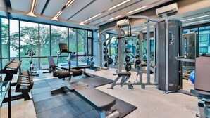 Un gimnasio moderno con varios equipos de ejercicio, ventanas amplias y una zona de bancos.