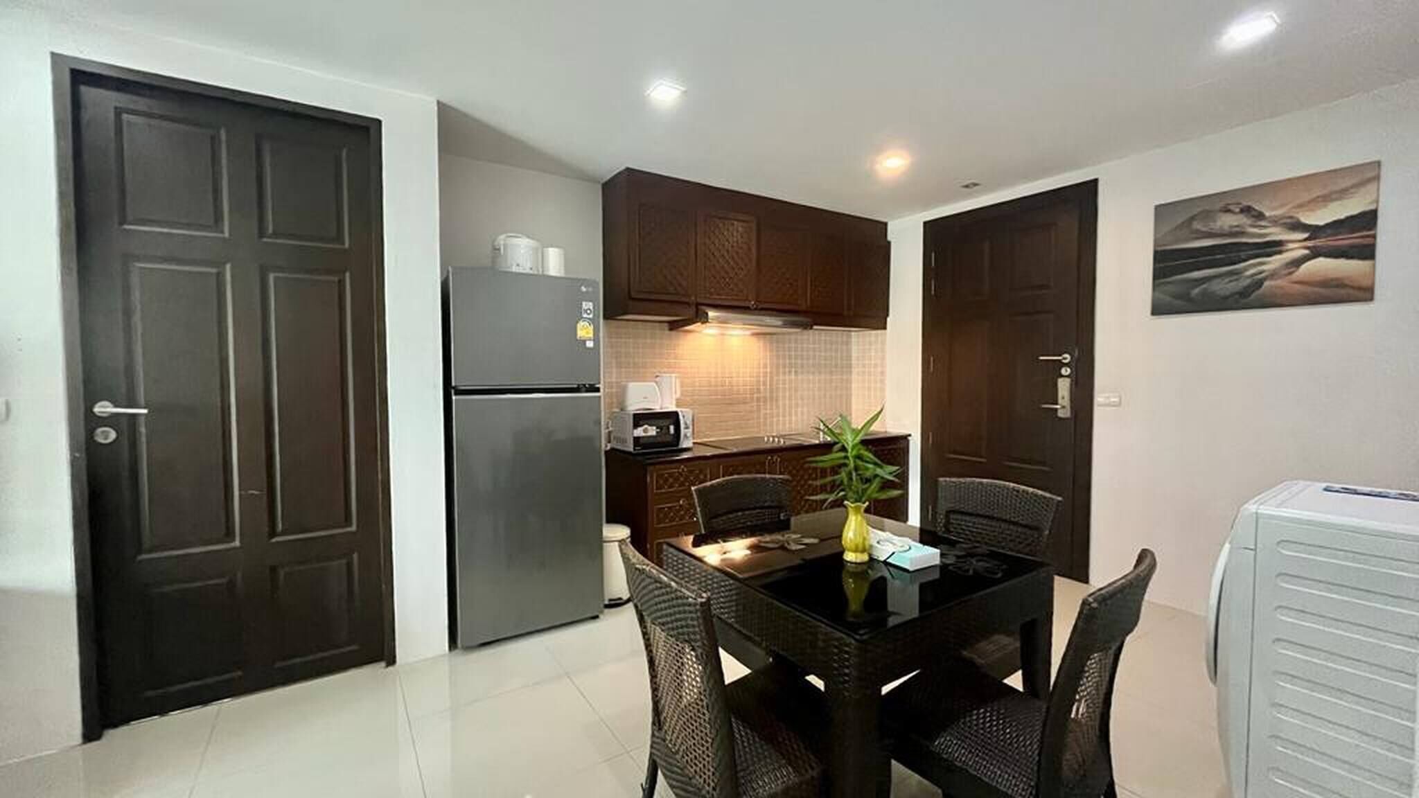 A compact kitchen with dark wooden cabinets, a refrigerator, a microwave, and a dining table with chairs.
