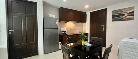 A compact kitchen with dark wooden cabinets, a refrigerator, a microwave, and a dining table with chairs.