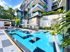A modern hotel with a swimming pool, lounge chairs, and a well-maintained garden.