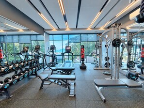 Un gimnasio con cintas de correr, mancuernas y máquinas de pesas, con amplias ventanas y vistas a las montañas.