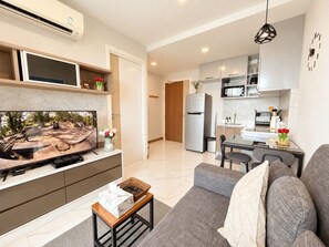 Una sala moderna con televisor de pantalla plana, un sofá, una mesa de centro y una zona de cocina con refrigerador, microondas y pileta.