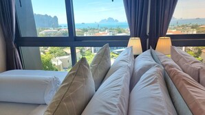 Camera d'albergo con una grande finestra che si affaccia sul mare e su isole all'orizzonte. Sono presenti diversi cuscini e un letto con copripiumino bianco.
