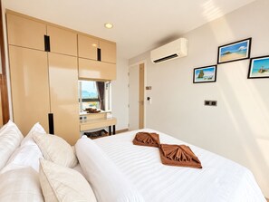 Habitación de hotel con cama, escritorio con espejo y armario. Hay cuadros en la pared y un equipo de aire acondicionado.
