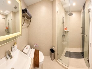 Un baño moderno con ducha de vidrio, un lavamanos blanco y un inodoro con una toalla encima.