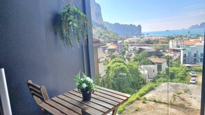 Un balcone con tavolo in legno e piante in vaso, con vista su una cittadina costiera, edifici e mare limpido.
