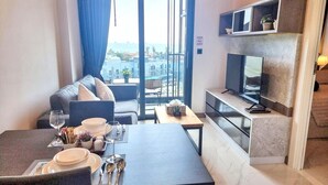 Een moderne hotelkamer met balkon, een zithoek met tafel gedekt voor twee personen, en een flatscreen televisie aan de muur.