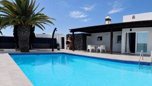 A swimming pool with a stone wall and a covered patio area with outdoor furniture. - Villa Descansa with private Pool, Air-Conditioning, Sea View, Smart-TV & Wifi (Montaña Roja)