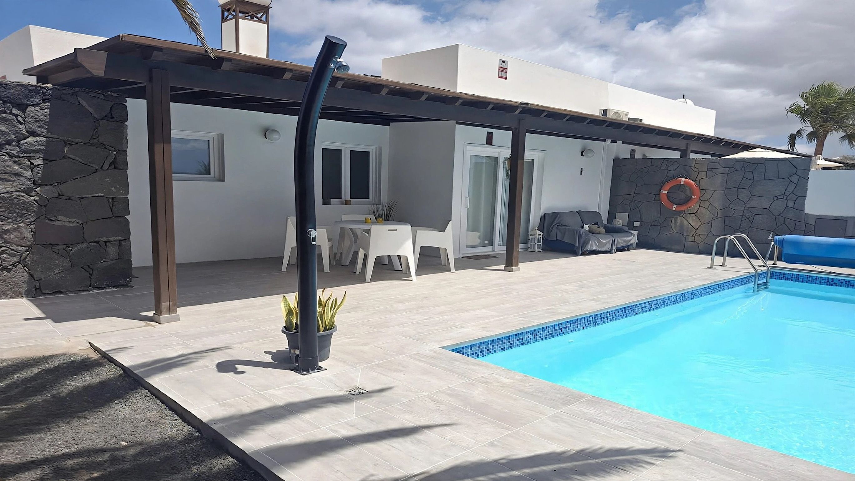 A poolside area with a covered patio, stone walls, and a lounge chair.