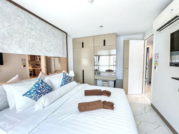 Quarto de hotel com cama, escrivaninha, espelho e televisão.