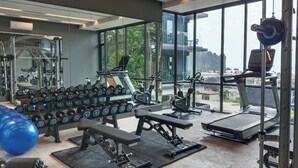 Un gimnasio moderno con varios equipos de ejercicio, ventanas amplias y vista a la ciudad.