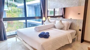 A hotel room with a large bed, a view of greenery outside, and a modern design.