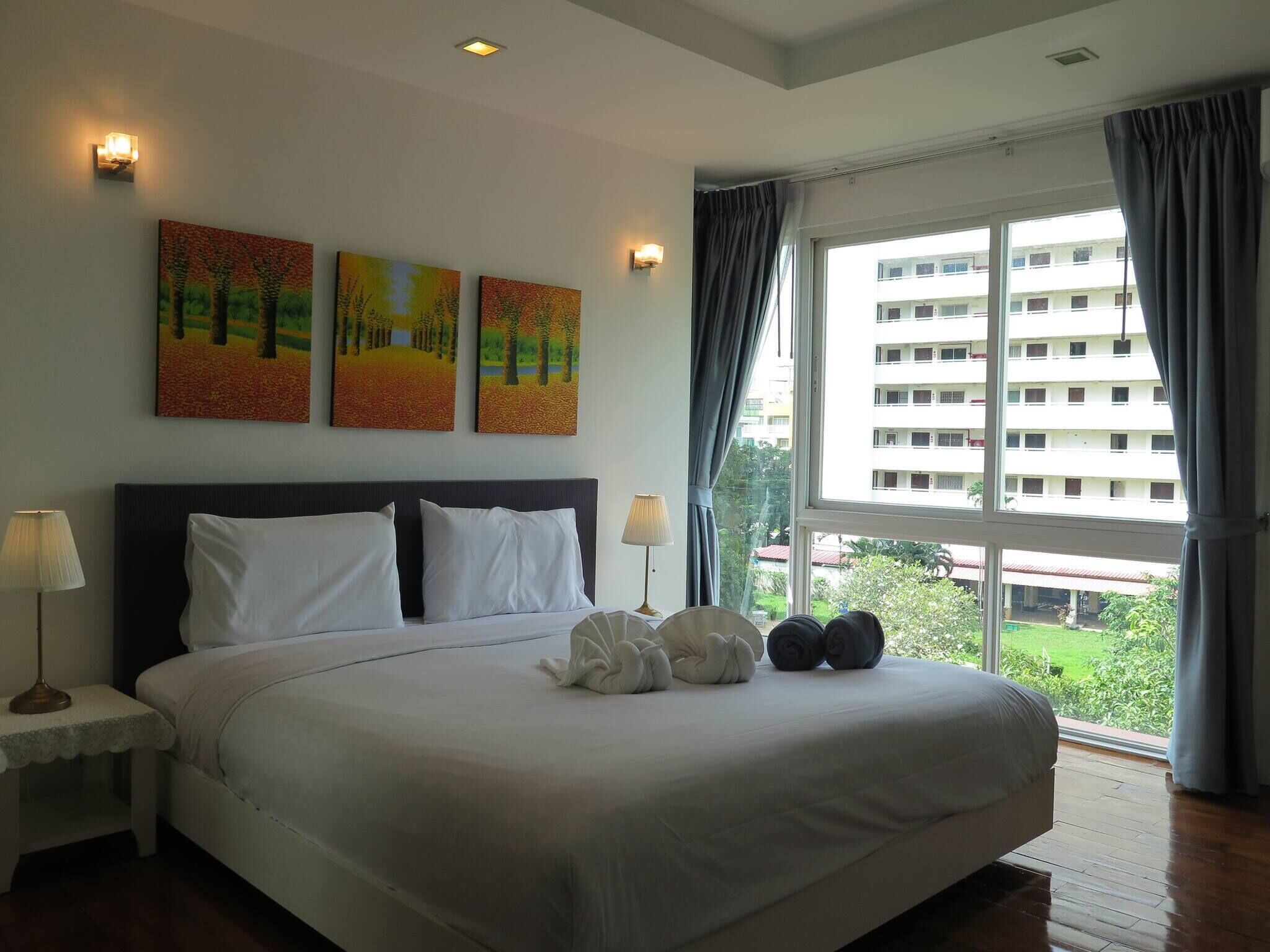 A hotel room with a large bed, two bedside tables, a window with curtains, and three paintings on the wall.