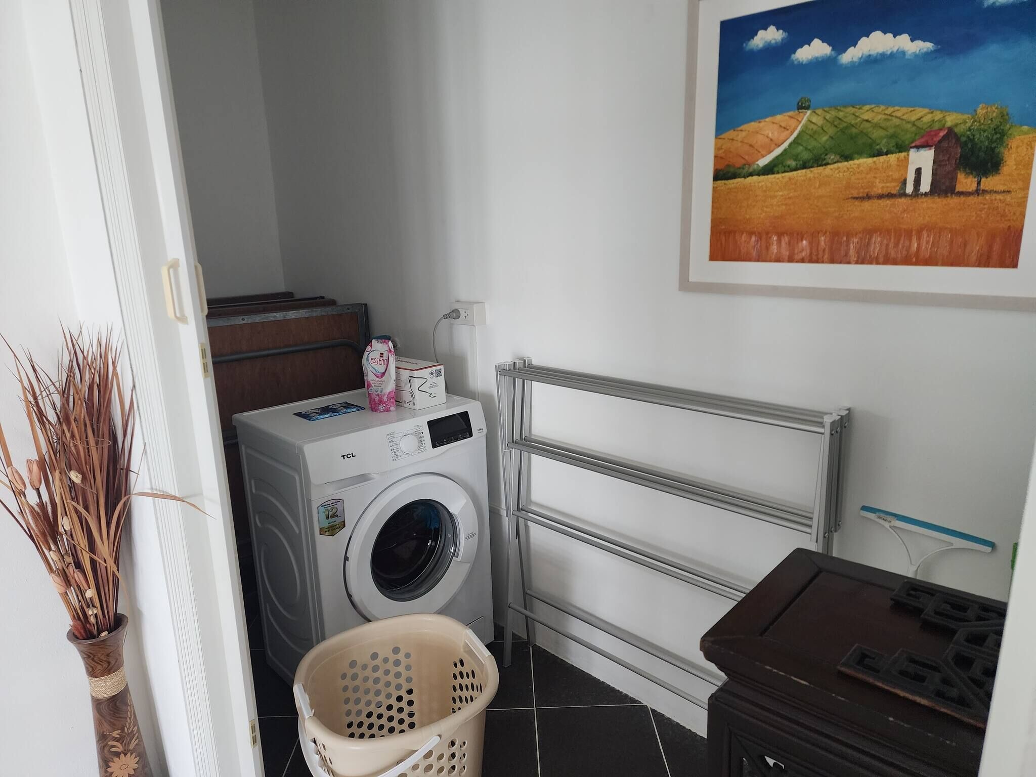 Een wasruimte met een voorlader wasmachine, een droogrek en een mand.