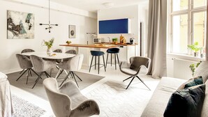 A modern living room with a dining area, a kitchen, and a large window with curtains.