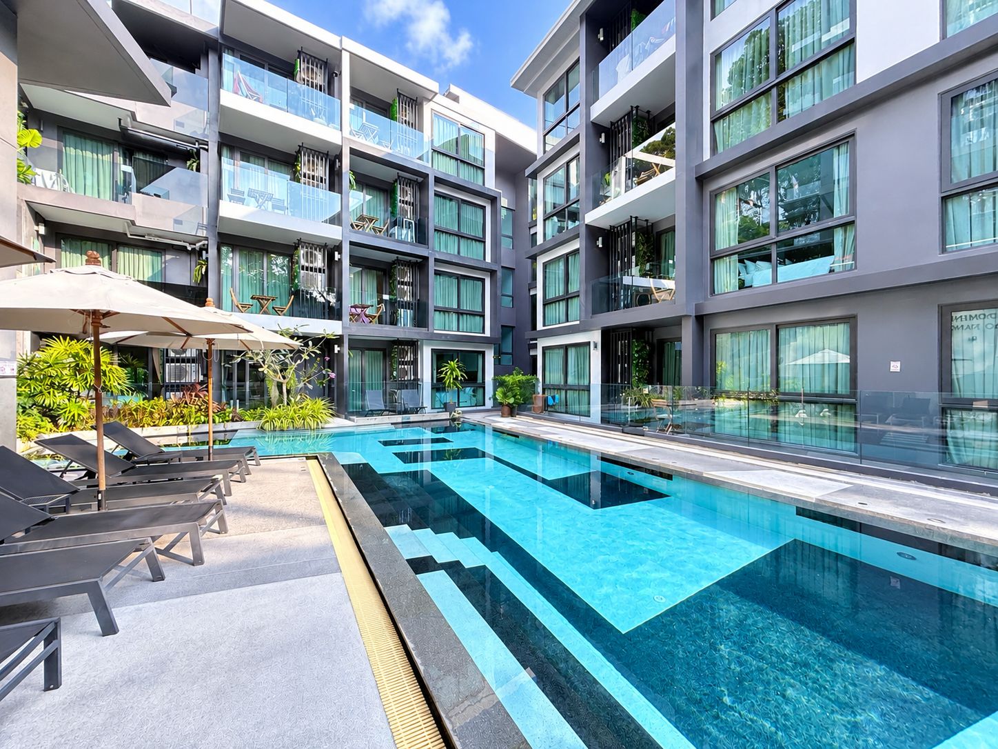 A modern hotel with a swimming pool, multiple balconies, and outdoor seating.