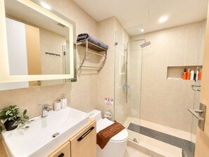 Un baño moderno con un espejo grande, un lavamanos, un inodoro y una zona de ducha.
