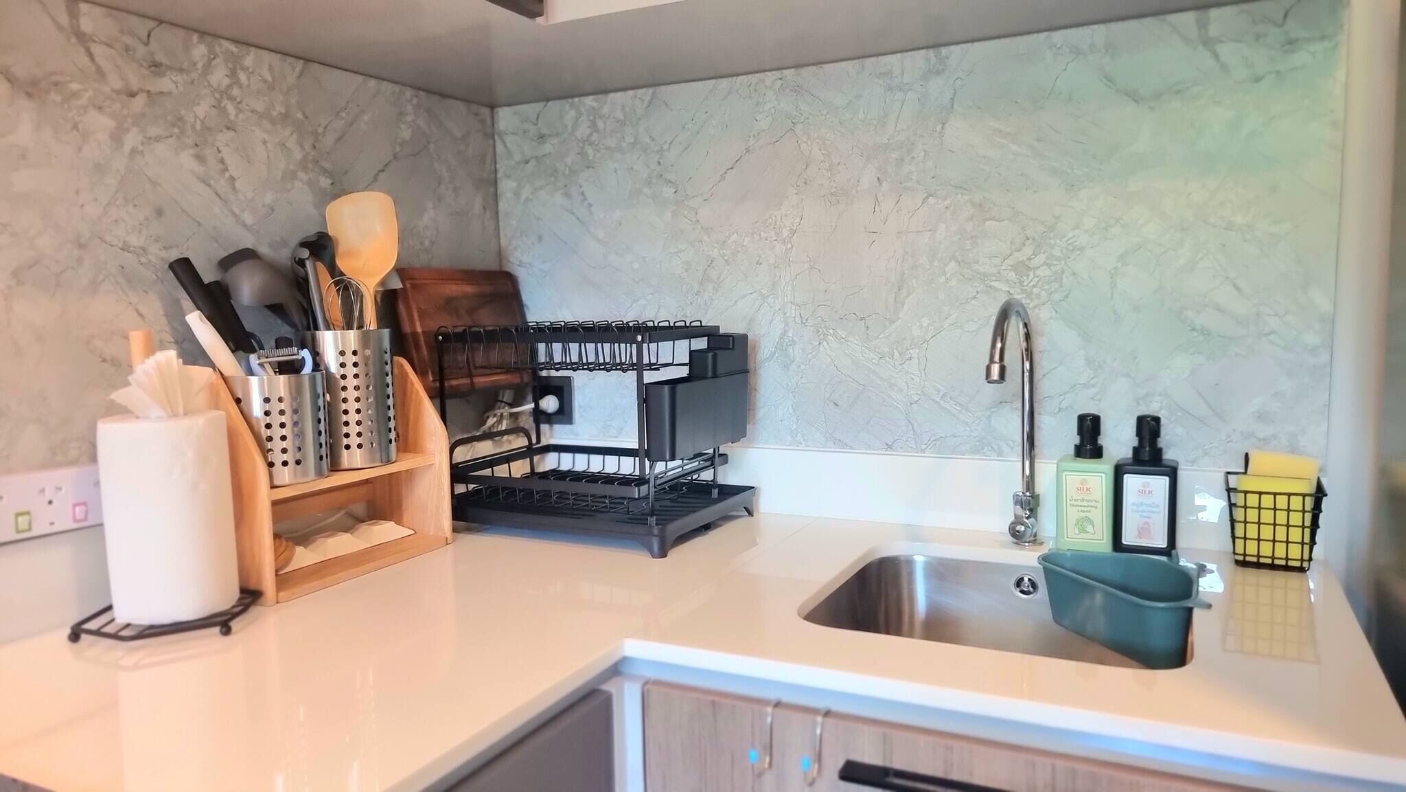 Uma cozinha moderna com painel de fundo de mármore, pia de aço inoxidável e utensílios e eletrodomésticos bem organizados.
