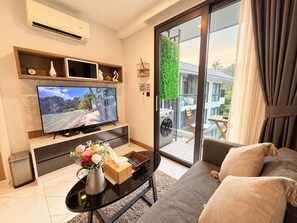Een moderne woonkamer met een flatscreen televisie, een bank, een salontafel en een balkon met uitzicht op een gebouw en groen.