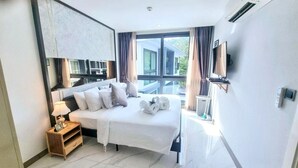 A modern hotel room with a bed, bedside table, lamp, and a large window with curtains. - B506 - 1 Bedroom Serviced Apartment Top Floor Pool View at Ao Nang Beach (Tambon Ao Nang)