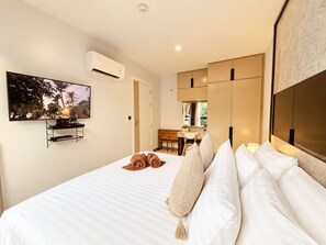 Una habitación de hotel con una cama, un televisor montado en la pared y una zona de kitchenette.