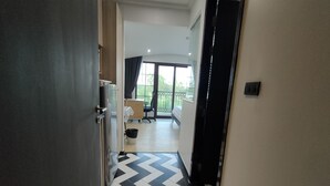 Un couloir d’hôtel avec un sol à carreaux, un lit, un bureau et une fenêtre donnant sur un paysage verdoyant.