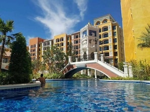 A hotel with a swimming pool, a bridge, and a multi-story building with balconies. - 422C - Luxury Studio Condo in Na Jomtien with Pool Access (Pattaya City)