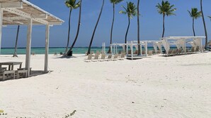 A beach with palm trees, a covered seating area, and a view of the ocean. - Spacious apartment w/private rooftop and private cool water jacuzzi  (Punta Cana)