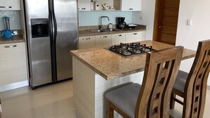 A modern kitchen with a stainless steel refrigerator, a gas stove, wooden chairs, and a coffee maker. - Spacious apartment w/private rooftop and private cool water jacuzzi  (Punta Cana)