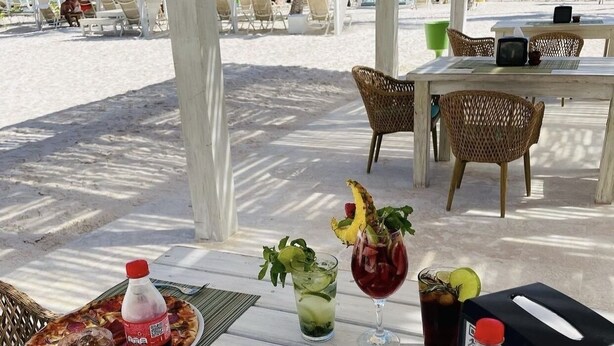 A beachside outdoor seating area with a table set for two, featuring a pizza, drinks, and a bottle of soda. - Spacious apartment w/private rooftop and private cool water jacuzzi  (Punta Cana)