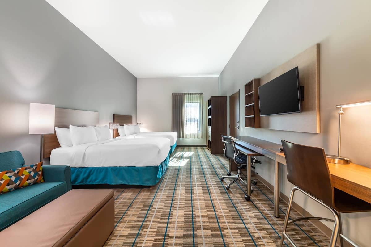 Habitación de hotel con una cama grande, un escritorio, una silla, un televisor y una ventana con cortinas.